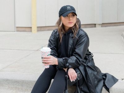 Hailie Jade is sitting on the concrete ground while holding a coffee.